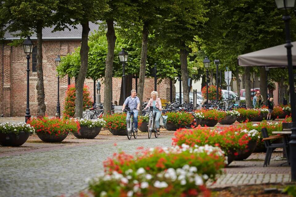 Twee mensen fietsen op een zonnige bloemrijke straat.