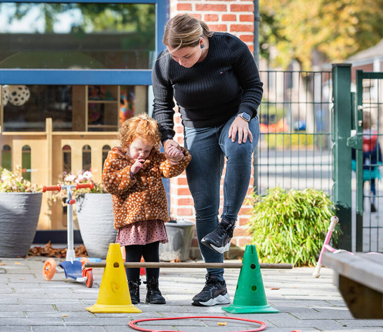 Volwassene helpt kind bij obstakelspel buiten.